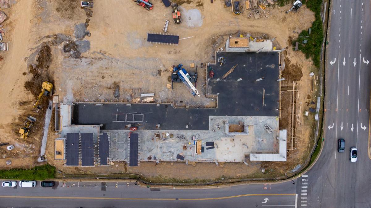 Aerial view of a construction site beside a road with marked turn arrows and a pedestrian crossing