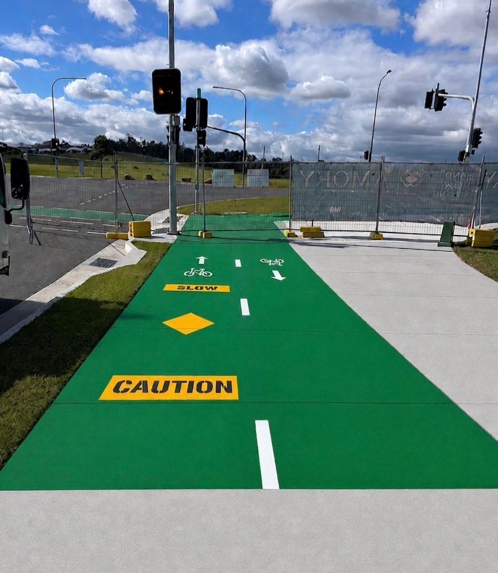 Green cycleway surfacing with directional arrows, bicycle symbols, centre lines and CAUTION and SLOW stencils at a signalised intersection